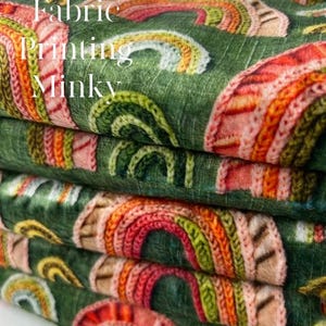 May include: A stack of Minky fabric with a repeating rainbow pattern in shades of red, orange, yellow, and green on a dark green background. The fabric has the words "Custom Fabric Printing Minky" printed on it.