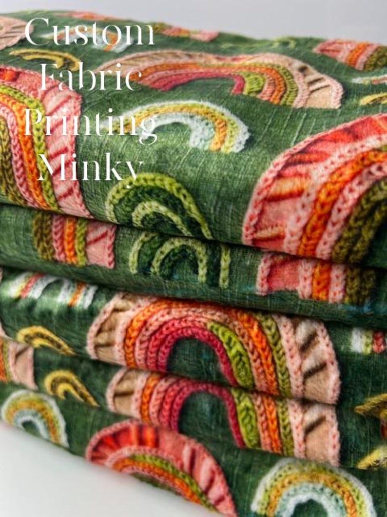 May include: A stack of Minky fabric with a repeating rainbow pattern in shades of red, orange, yellow, and green on a dark green background. The fabric has the words "Custom Fabric Printing Minky" printed on it.