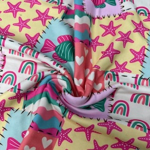 May include: A colorful fabric with a patchwork design featuring pink starfish, fish, rainbows, and hearts. The fabric has a variety of colors including pink, yellow, blue, and white. The design is reminiscent of a nautical or beach theme.