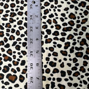 May include: Cream-colored fabric with a leopard print pattern featuring black and brown spots. A metal ruler, marked in inches, is placed vertically on the fabric, showing measurements from 28 to 35 inches.
