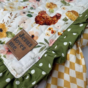 May include: A quilted, floral-patterned fabric with a brown chicken illustration and the text "Jesus loves me." The fabric has a green polka-dot ruffle and a yellow and white checkered pattern.