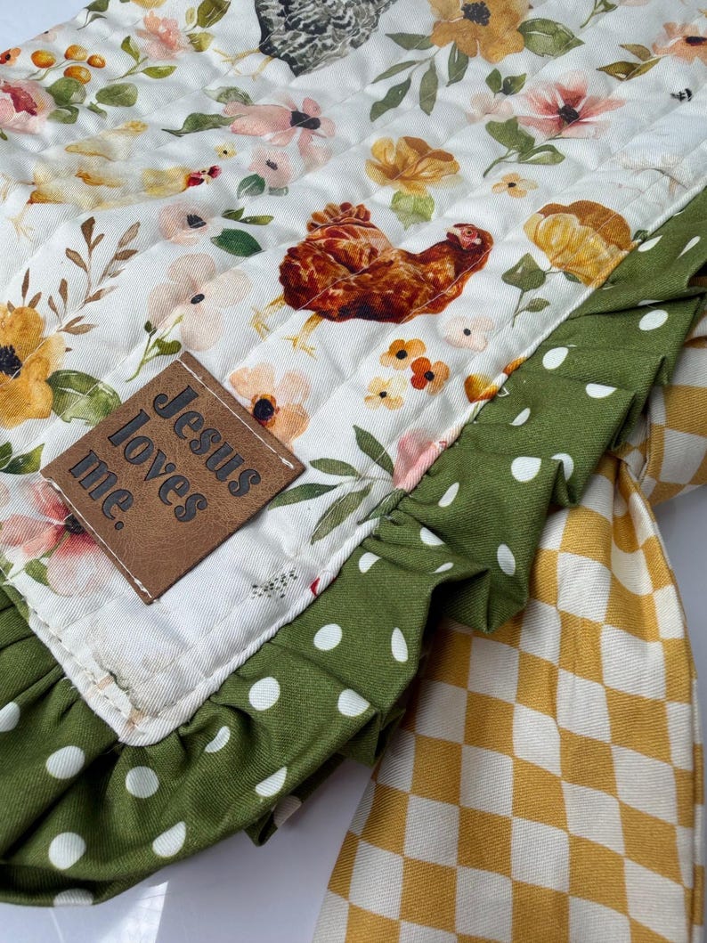 May include: A quilted, floral-patterned fabric with a brown chicken illustration and the text "Jesus loves me." The fabric has a green polka-dot ruffle and a yellow and white checkered pattern.
