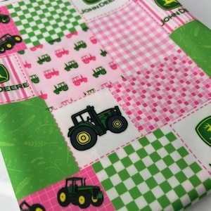 May include: A patchwork fabric featuring green, pink, and white squares. The design includes gingham, tractor graphics, and the John Deere logo. The fabric is folded, showing a variety of patterns and colors.