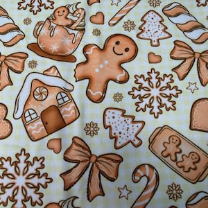 May include: A festive fabric pattern featuring gingerbread men, gingerbread houses, snowflakes, bows, candy canes, and Christmas trees in shades of brown and white on a light yellow checkered background. The design is perfect for holiday-themed crafts.