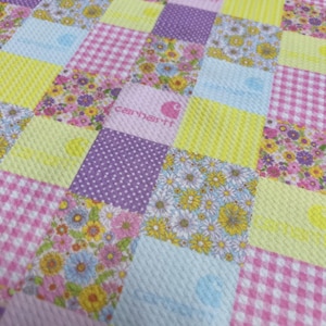May include: A patchwork fabric with a variety of patterns, including floral, gingham, and polka dots. The fabric is in shades of pink, yellow, purple, and blue. The Carhartt logo is visible in the center of the fabric.