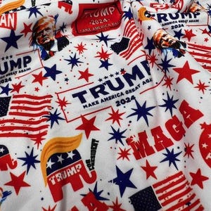 May include: White fabric with a repeating pattern of red, white, and blue stars, American flags, and the text "TRUMP" and "MAGA". Includes a portrait of a man and the text "MAKE AMERICA GREAT AGAIN 2024".