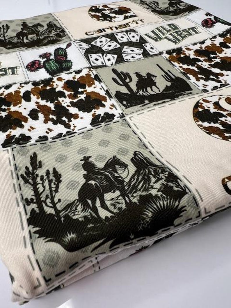 Op de afbeelding: Een witte stof met een patchwork-ontwerp met cowboys, paarden, cactussen en speelkaarten. De stof heeft een bruin, groen en zwart kleurenschema. De tekst "Wild West" en "Carhartt" is zichtbaar op de stof.