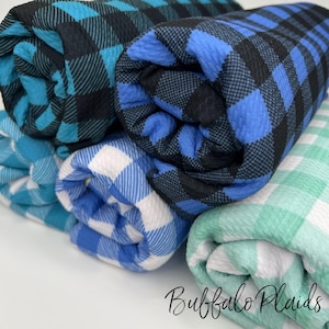 May include: Four rolls of buffalo plaid fabric in various colors, including teal, blue, white, and green. The fabric is folded and rolled up, showing the plaid pattern.
