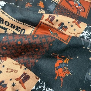 May include: Fabric with a patchwork design featuring rodeo-themed illustrations. The fabric includes images of cowboys, bulls, boots, and the word "RODEO" in a stitched-style font. The color palette includes black, brown, and tan.