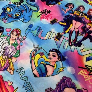 May include: A vibrant fabric featuring a repeating pattern of anime-style illustrations. The design includes characters, a blue tiger, hearts, diamonds, and the text "Sija Boys" and "Huntra" in a graffiti style. The background is a mix of blue, pink, and yellow.