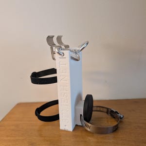 以下が含まれることがあります： 金属製のクランプ、黒いストラップ、金属リングを備えた白い3Dプリントデバイス。 「3DMESH.NET」の文字が側面に縦に印刷されています。 このデバイスは、オブジェクトを保持するように設計されています。