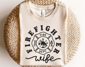 May include: A beige t-shirt with a black firefighter emblem and the text "FIRE DEPT. wife" printed on the front.