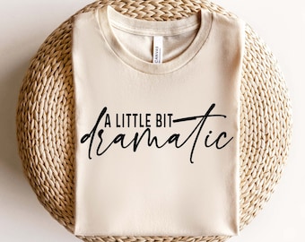 May include: A beige t-shirt with the text "A little bit dramatic" printed in black.