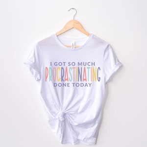 Peut inclure: T-shirt blanc avec un graphique arc-en-ciel qui dit "J'ai tellement procrastin&eacute; aujourd'hui."