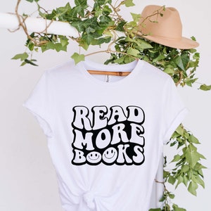 May include: White t-shirt with a black graphic that says "Read More Books" in a retro font with smiley faces.