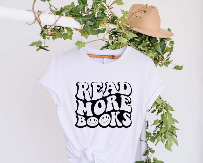 May include: White t-shirt with a black graphic that says "Read More Books" in a retro font with smiley faces.