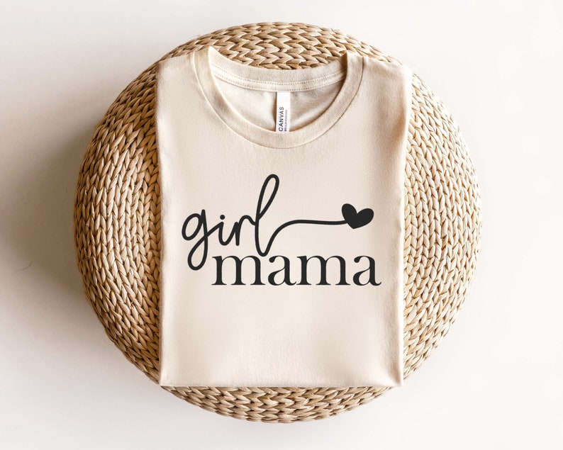May include: A beige t-shirt with the text "girl mama" in black lettering and a small black heart.