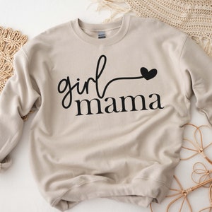 May include: A beige sweatshirt with the text "girl mama" in black lettering and a small black heart.
