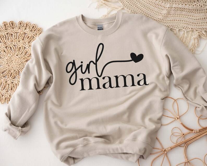 May include: A beige sweatshirt with the text "girl mama" in black lettering and a small black heart.