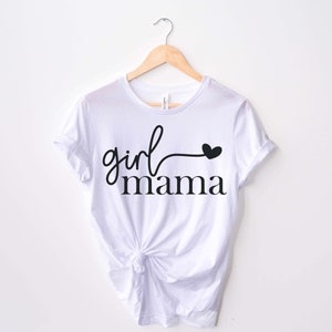 May include: White t-shirt with black text that reads "girl mama" with a small heart at the end of the word "girl".