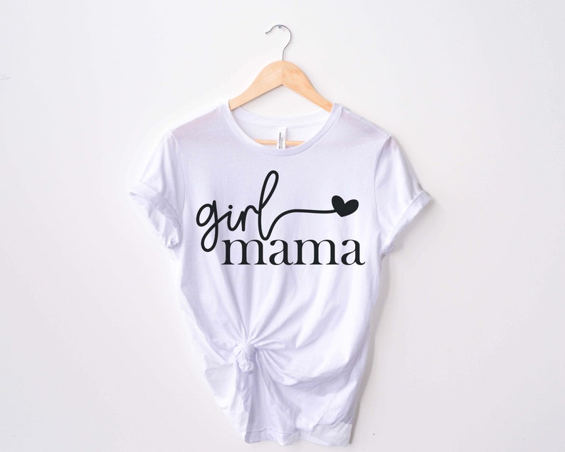 May include: White t-shirt with black text that reads "girl mama" with a small heart at the end of the word "girl".