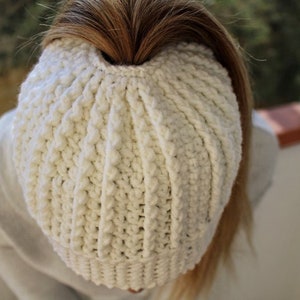 Op de afbeelding: Een witte gehaakte beanie met een gat bovenop voor een paardenstaart.