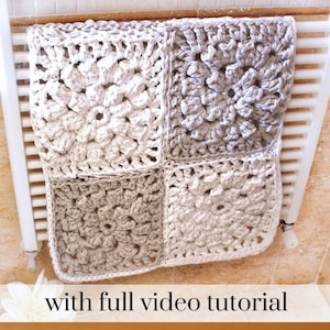Puede incluir: Una manta cuadrada de ganchillo hecha a mano en tonos crema y gris, compuesta por cuatro grandes cuadrados de la abuela. La manta está colocada sobre un radiador blanco. El texto "with full video tutorial" es visible en la parte inferior.