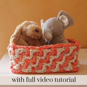 May include: A rectangular, handmade crochet basket in coral and white chevron pattern. The basket contains a plush brown bunny and a gray elephant toy. The text "with full video tutorial" is at the bottom of the image.