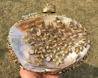 May include: A gold and white shell clutch with a floral design. The clutch has a gold clasp and is decorated with small white pearls.