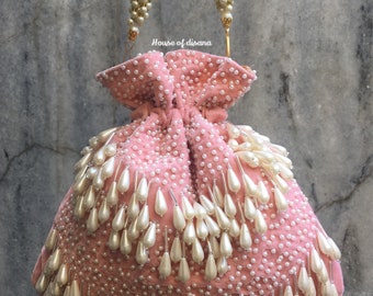 May include: A pink velvet drawstring bag with a gold chain handle and a fringe of white pearl beads. The bag is decorated with white pearl beads.