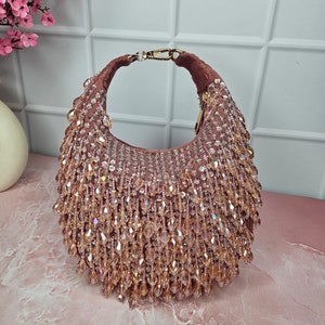 May include: A blush pink handbag with a gold chain strap and a fringe of iridescent crystals.