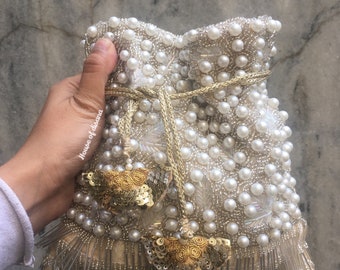 May include: A white beaded drawstring bag with gold sequins and fringe. The bag has a tassel with a gold sequin design.