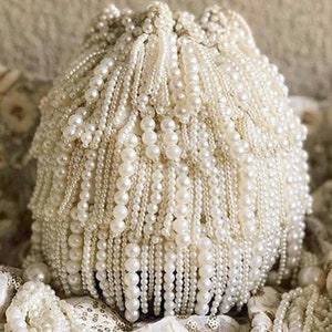 Könnte beinhalten: Ein weißer Perlenkugelschmuck aus vielen Perlensträngen. Der Schmuck ist rund und hat eine glatte Oberfläche. Es ist ein dekoratives Element, das für verschiedene Zwecke verwendet werden kann.