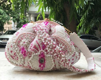 May include: A white and pink beaded clutch bag with a gold clasp and a white strap. The bag is decorated with pink and white beads and has a floral design.