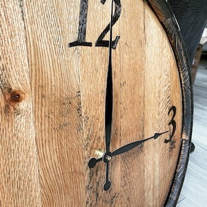 May include: A wooden clock face with black Roman numeral markings for 12 and 3. The clock hands are black and the clock is mounted on a wooden barrel.