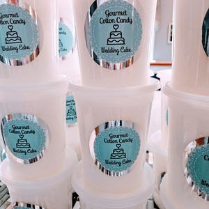 May include: Multiple white plastic containers with lids, each containing cotton candy. The containers have silver labels with a blue and white design that reads "Gourmet Cotton Candy Wedding Cake".