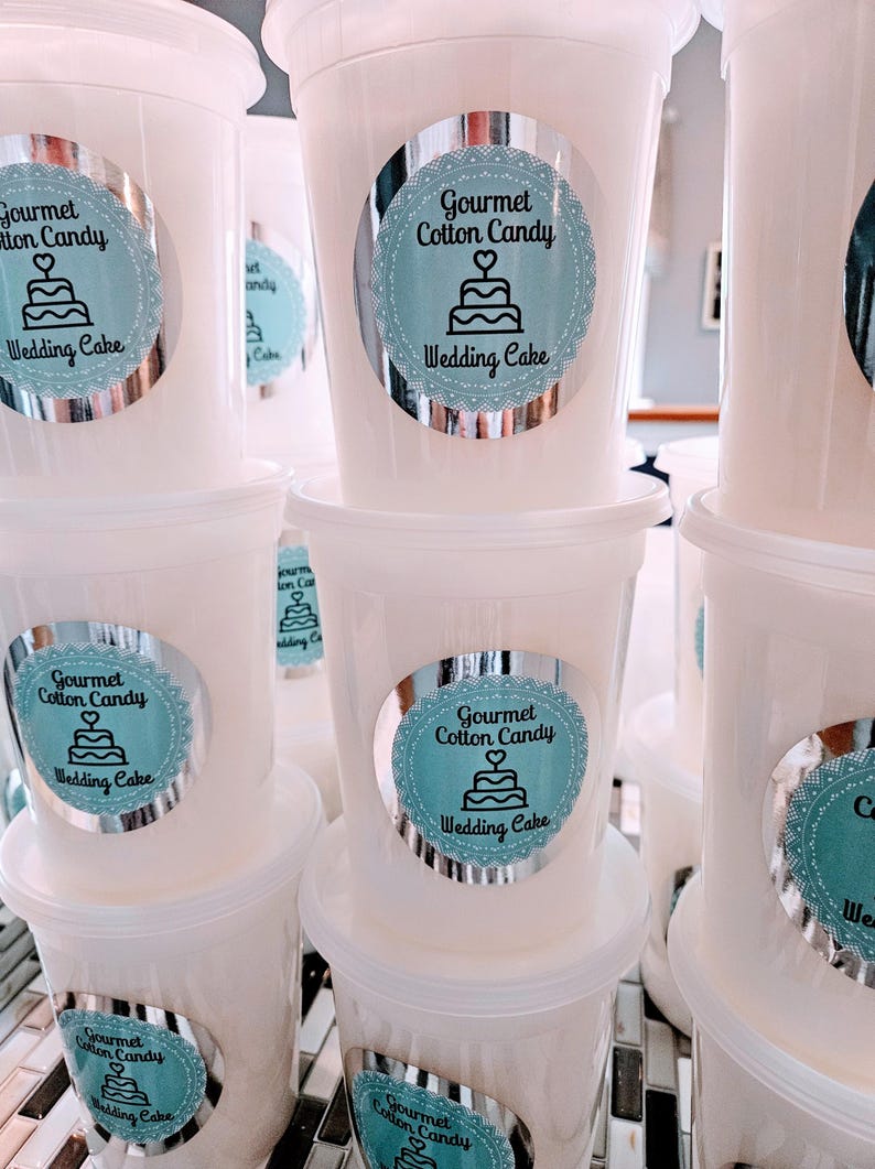 May include: Multiple white plastic containers with lids, each containing cotton candy. The containers have silver labels with a blue and white design that reads "Gourmet Cotton Candy Wedding Cake".