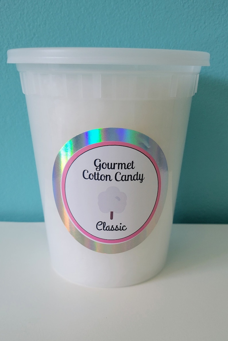 May include: A white plastic container with a lid, filled with white cotton candy. The container has a holographic sticker with the text "Gourmet Cotton Candy" and "Classic" in pink and white.