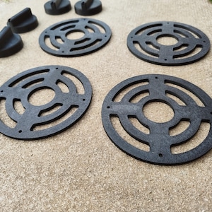 Puede incluir: Colección de objetos circulares negros con una serie de anillos concéntricos y diseños recortados. También hay varias piezas negras angulares más pequeñas. Los artículos parecen estar hechos de un material texturizado.
