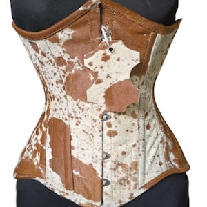 May include: A brown and white cowhide corset with a metal zipper and a leather tag. The corset has a pointed bottom and a lace-up back.