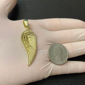 May include: A gold-tone angel wing pendant charm. The wing is detailed with a textured pattern and is shown next to a US quarter for size comparison.