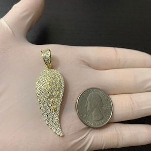 May include: Gold-tone pendant featuring a single angel wing design with clear cubic zirconia stones. The pendant is shown next to a US quarter for size comparison.