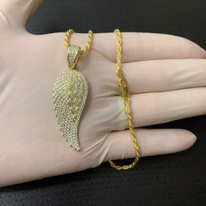 May include: A gold chain necklace with a large, diamond-encrusted angel wing pendant. The chain is a rope style and the pendant is a single wing.