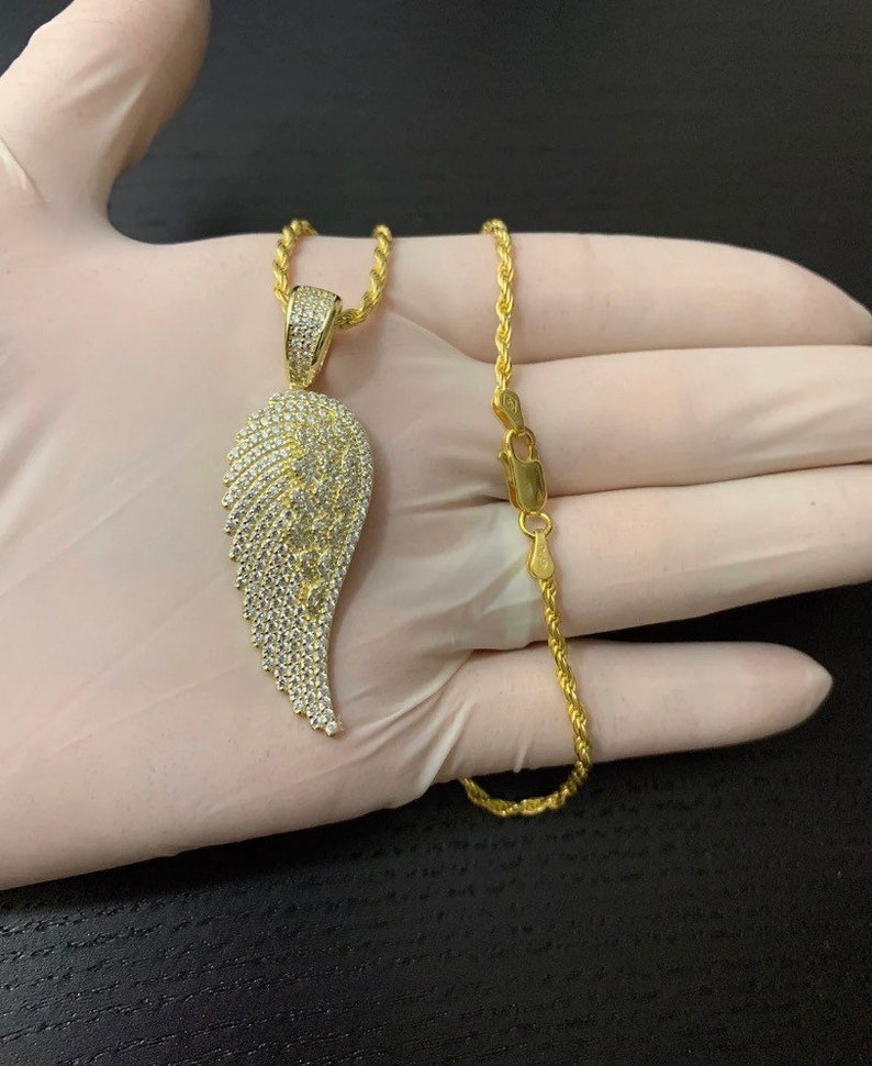 May include: A gold chain necklace with a large, diamond-encrusted angel wing pendant. The chain is a rope style and the pendant is a single wing.