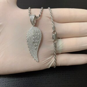 May include: A silver chain necklace with a large, silver, diamond-encrusted angel wing pendant.