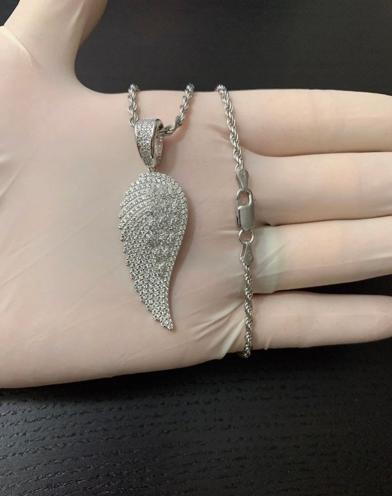May include: A silver chain necklace with a large, silver, diamond-encrusted angel wing pendant.