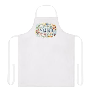 Op de afbeelding: Witte schort met een bloemenontwerp en de tekst "I will bless the LORD at all times". Het ontwerp bevat kleurrijke bloemen en bladeren. De schort heeft een nekband en taillebanden.
