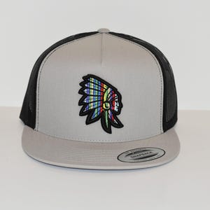 May include: A gray and black trucker hat with a colorful embroidered Native American headdress design. The hat has a black mesh back and a gray front panel. The hat is a snap back style.