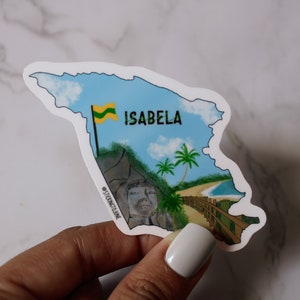 May include: A sticker depicting the island of Isabela, Dominican Republic. The sticker features a blue sky with white clouds, a green flag, a palm tree, a beach, and a stone face. The text "ISABELA" is printed on the sticker.