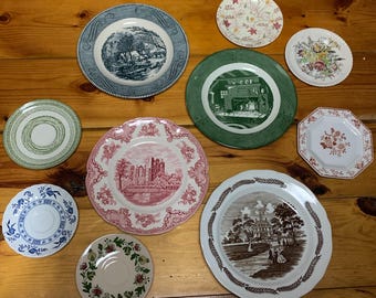 May include: A collection of ten decorative plates with various designs and colors. The plates feature floral patterns, landscapes, and architectural details.